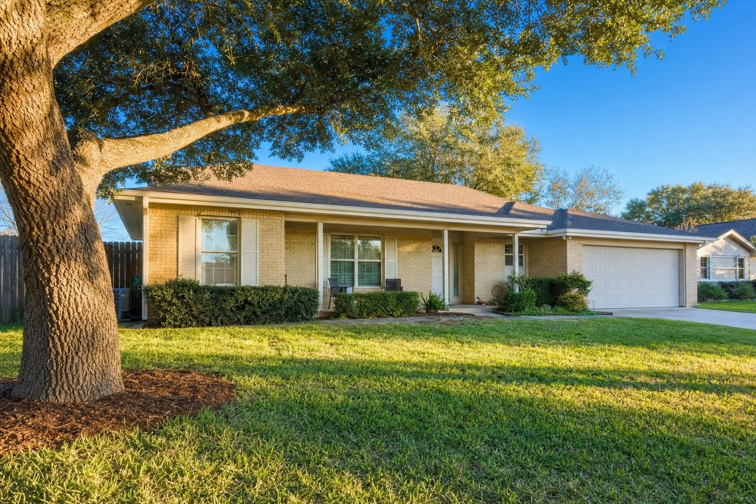 A single-story Texas suburban home with a covered front porch and mature oak tree